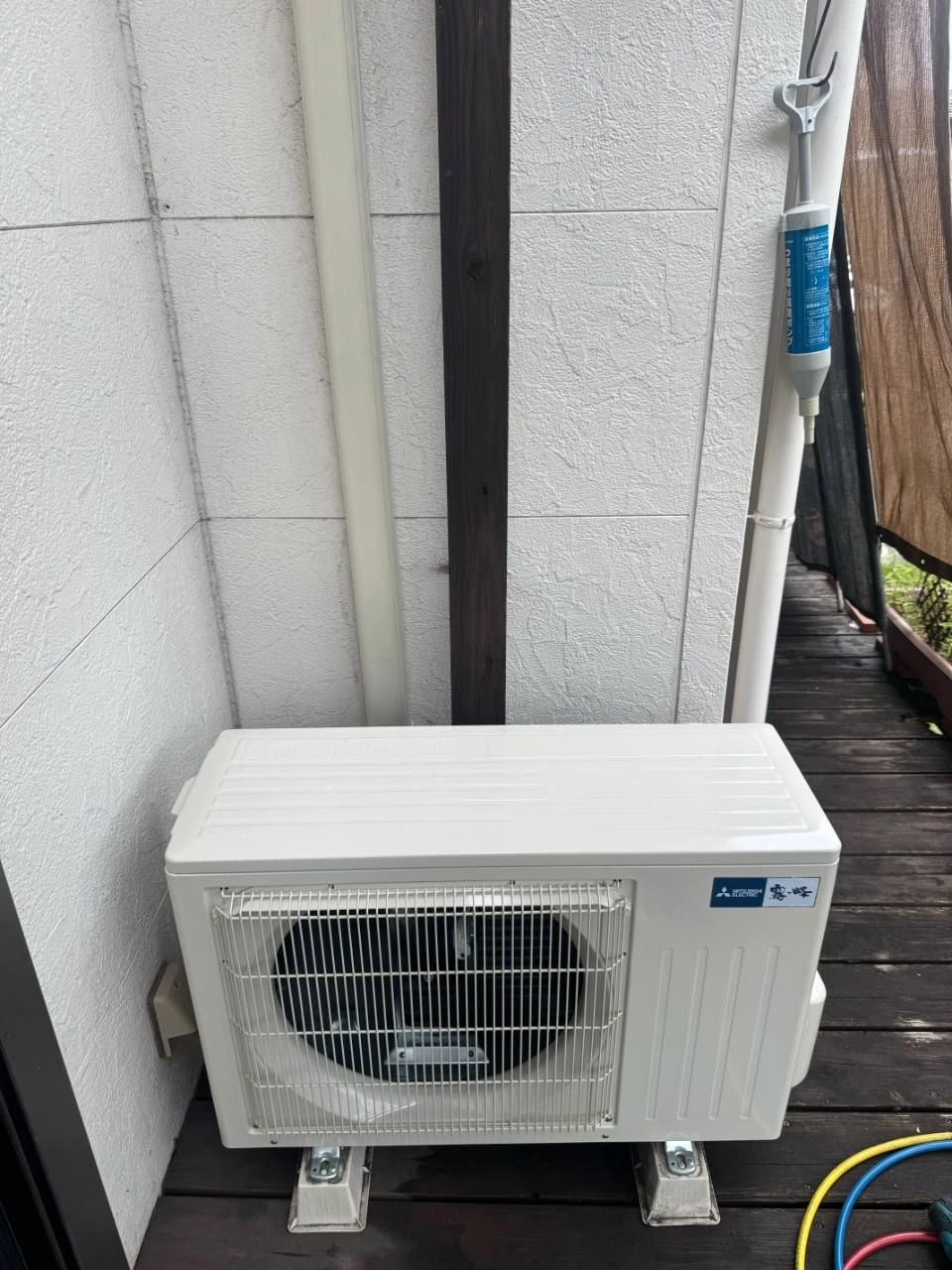 屋外の木製床面に設置された三菱電機の室外機と壁面の配管カバー